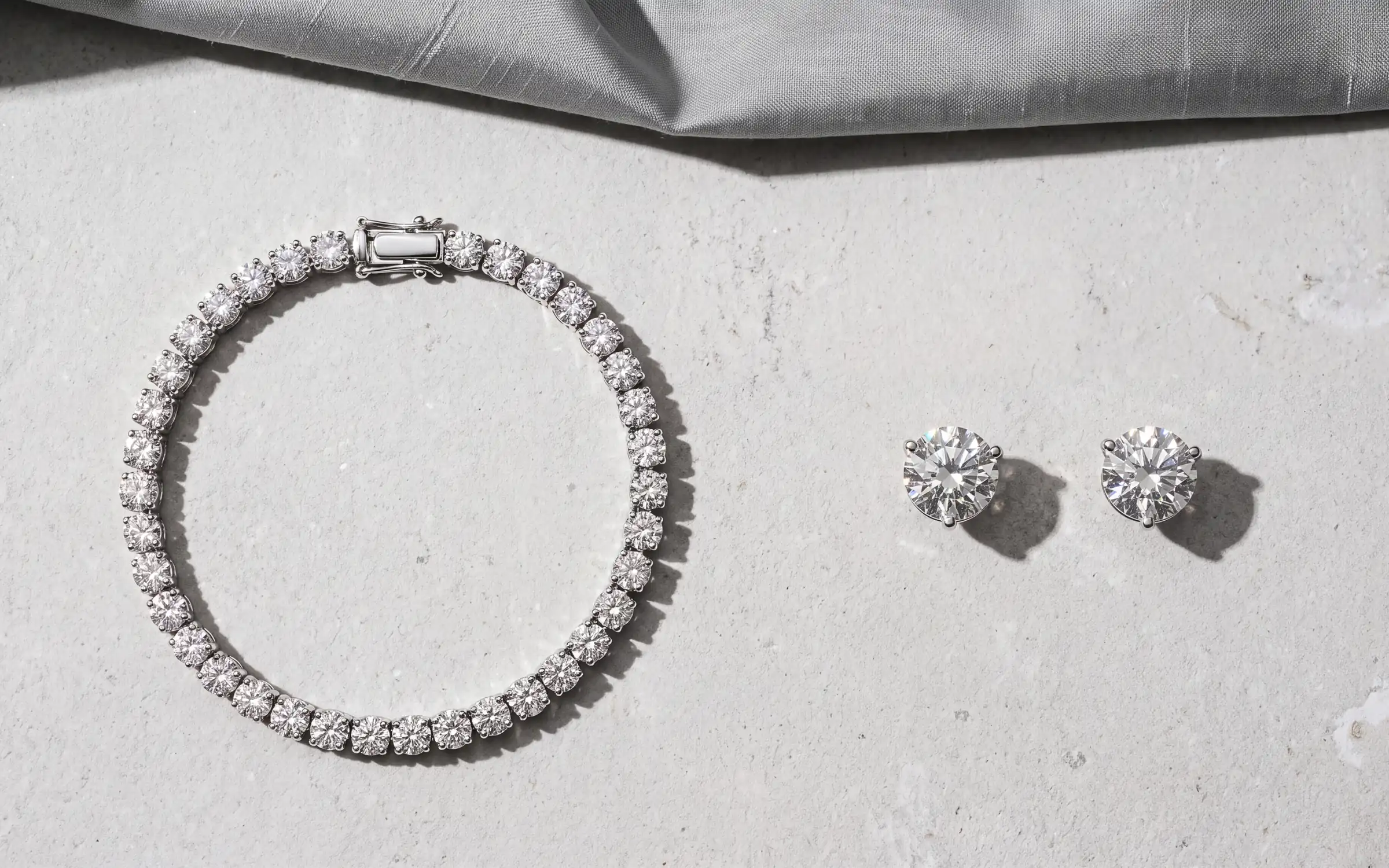 Diamond tennis bracelet and diamond stud earrings in a flat lay on limestone, made with Aurix