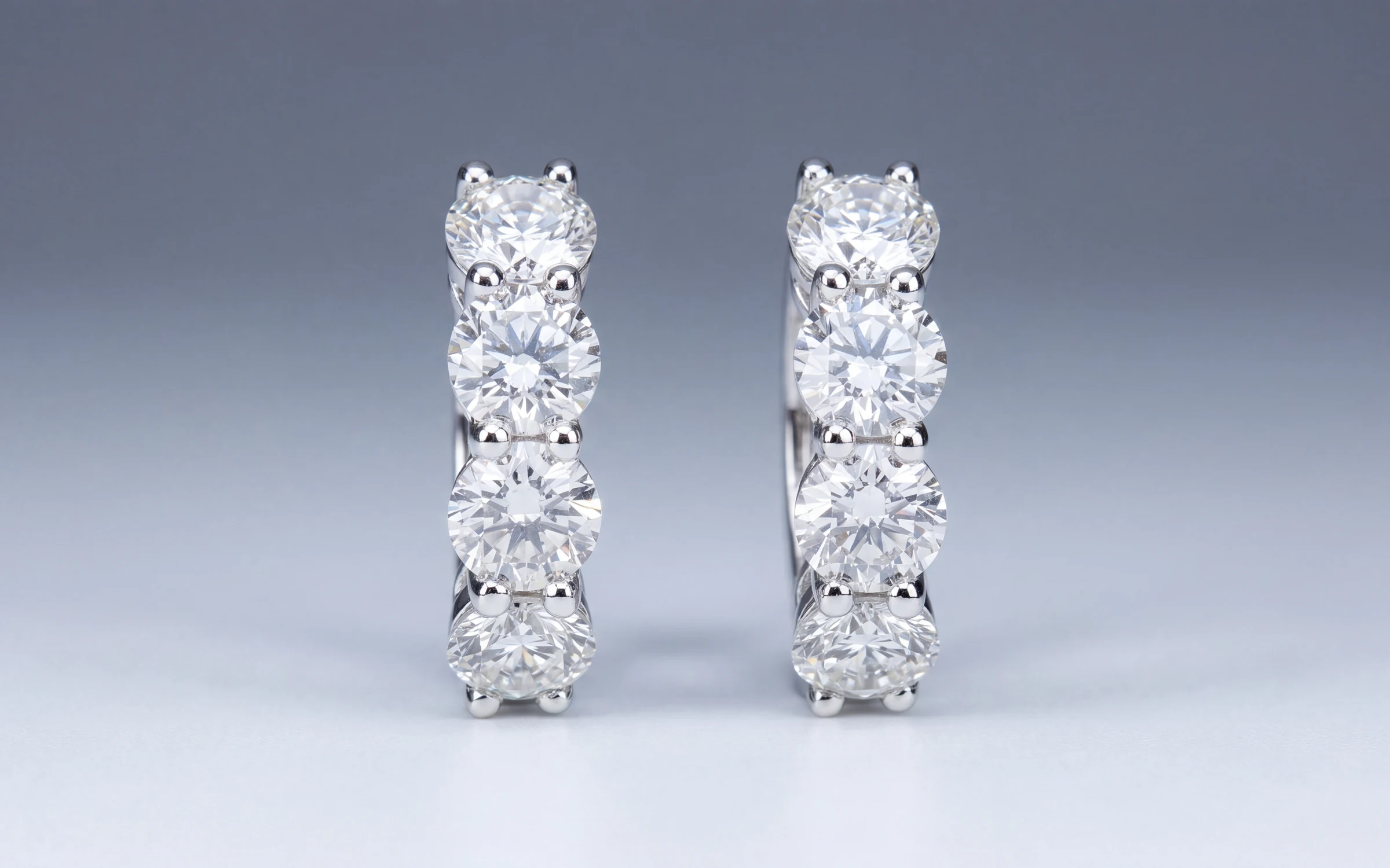 A pair of four-diamond huggie earrings on a cool grey backdrop, made with Aurix